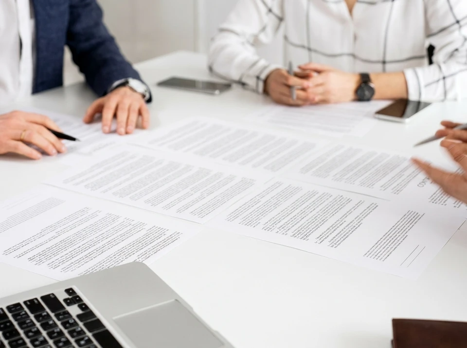 Réunion d'affaires autour d'une table en bois clair avec deux personnes analysant des documents contractuels et graphiques